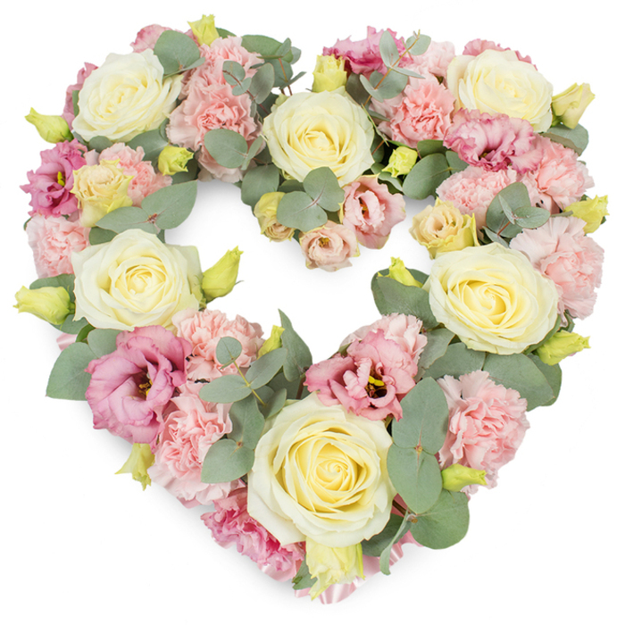 Set against a bright, uncluttered white background, a meticulously crafted heart-shaped wreath appears rich and full, every inch covered in flowers and foliage. The heart is clearly defined, its curves created by a tapestry of soft pastel petals and cool green leaves. Large, creamy ivory and pale yellow roses serve as anchors within the design, each bloom carefully positioned so that their velvety, swirling centres draw the eye around the heart. Filling the spaces between them, clusters of ruffled pastel pink carnations provide a gentle, cushiony texture, their layered petals giving the arrangement a plush, comforting appearance. Scattered throughout are deeper pink, almost mauve, lisianthus blossoms, their more open, trumpet-like forms introducing a touch of drama and emotional intensity without breaking the wreath's soothing harmony. Eucalyptus foliage is threaded through the flowers, its rounded, silvery-green leaves adding depth, contrast, and a sense of calm reminiscent of quiet walks through New Addington's green spaces. Small yellow-green buds peek out here and there, suggesting new life and the hope that memories endure. The density of the flowers gives the piece a luxurious, hand-crafted feel, as though a skilled local florist has taken time to honour a unique life with every stem. This heart-shaped tribute would be fitting for a funeral or memorial, perhaps resting beside a photograph at a service, or placed at a graveside after a farewell gathering. Its palette of creams, pinks, and soft greens conveys love, remembrance, and gentle sympathy, offering a serene, dignified way for families in New Addington to express their condolences and celebrate a life well-lived.